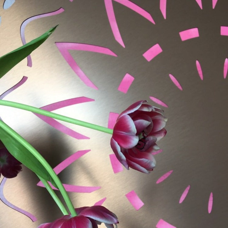 Close-up of the KuvaLight New Beginning design lamp in brushed gold. The pink color of the light fits the pink tulips standing in front of the KuvaLight.